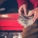 Man holding cash in front of a red car